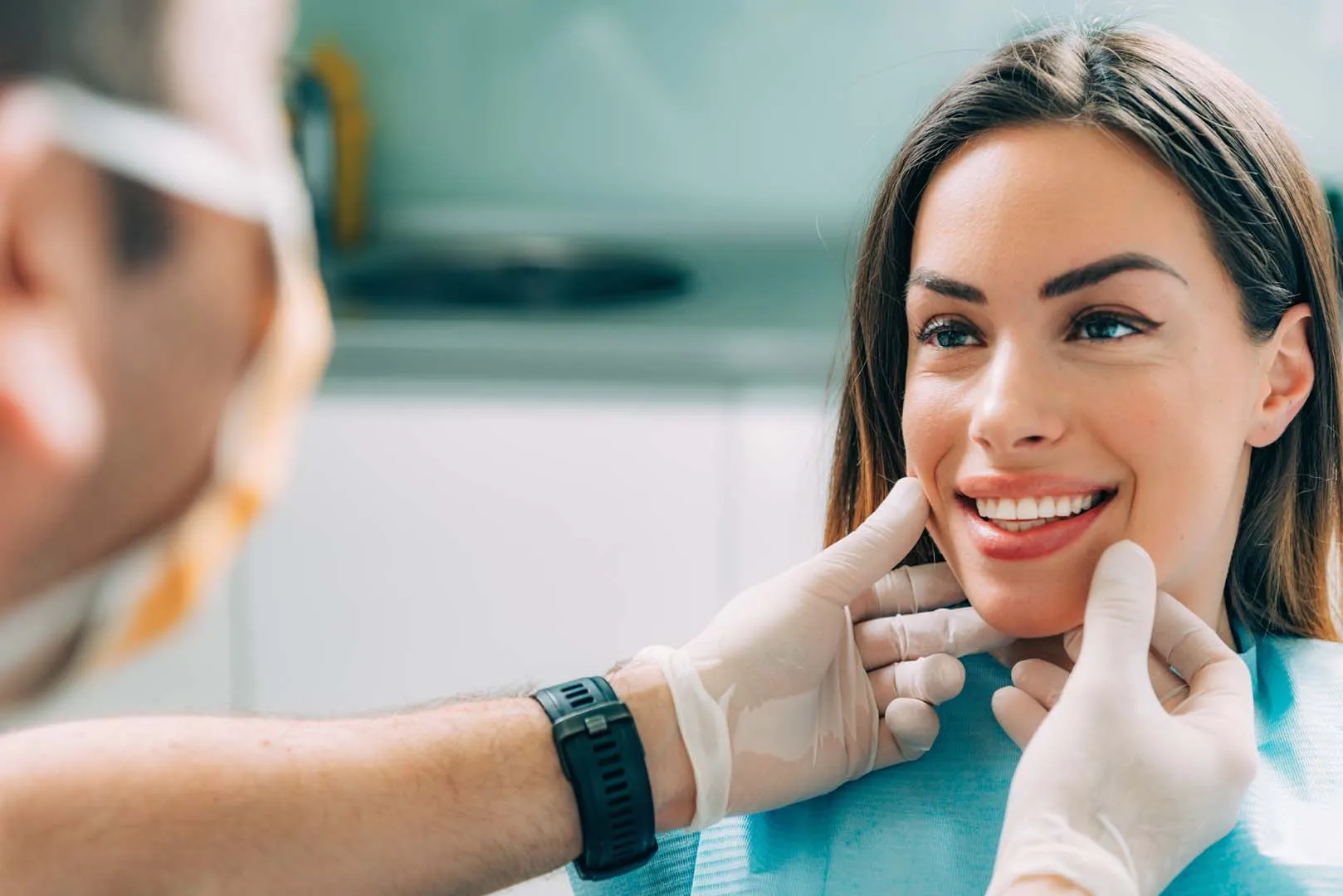 Dentist with gloves examining a smiling woman's teeth in a dental clinic.