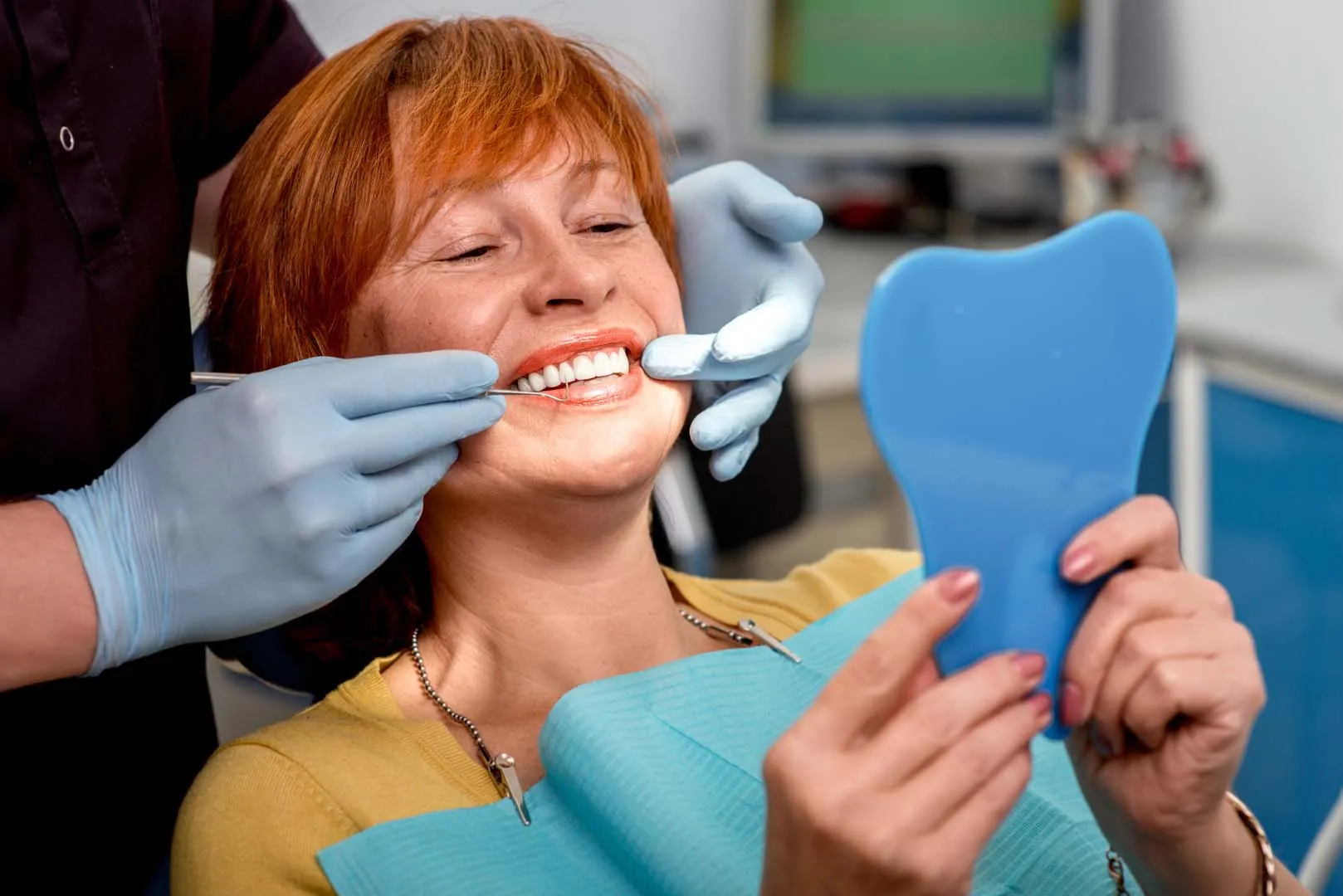 Woman smiling in dental chair while dentist flosses her teeth.